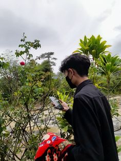 a man wearing a face mask looking at his cell phone in front of some trees