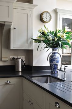 a blue and white vase with flowers in it sitting on a kitchen counter next to a clock