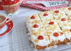 a cake with white frosting and cherries on it next to a cup of coffee