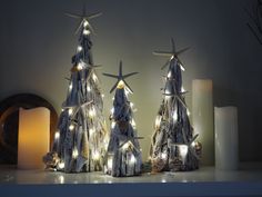 three wooden christmas trees with lights on them and candles in front of the top one