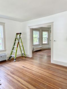 an empty living room with hard wood floors and ladders on the wall next to it