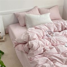 an unmade bed with pink sheets and headphones on the pillowcase, next to a potted plant