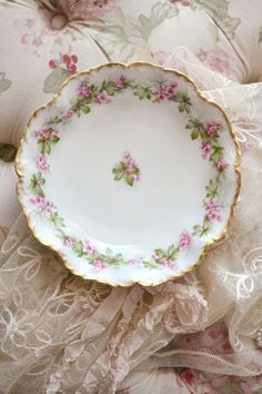 a white plate with pink and green flowers on it sitting on a lace covered surface