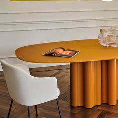 an orange table with two white chairs and a book on it