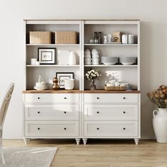 an empty room with white furniture and flowers in vases on the table, next to a large open bookcase