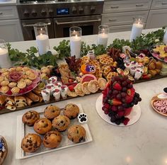 a table filled with lots of food on top of a white counter next to candles