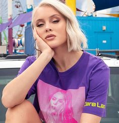 a woman sitting on the hood of a car wearing a purple t - shirt and jeans