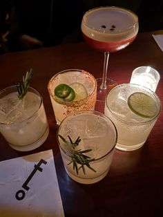 three different cocktails sitting on top of a wooden table next to glasses filled with drinks