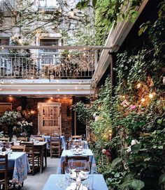 an outdoor restaurant with tables and chairs covered in blue tablecloths, surrounded by greenery