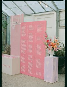 pink and white wedding seating plan displayed in front of flower arrangement on display box with flowers