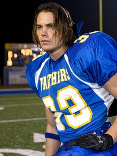 a football player is sitting on the sidelines with his hands in his pockets and looking at the camera