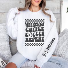 "Stay cozy and stylish on the sidelines with our personalized soccer mom crewneck sweatshirt! The front features a retro-inspired \"weekends, coffee, soccer, repeat\" text, perfect for every soccer mom out there. On the left sleeve, you'll find a design showcasing your kid's name and their jersey number, adding a special touch to this already unique piece. Whether you're cheering on your little star or running errands, this sweatshirt is a must-have for any soccer mom who wants to show off their pride in style. *All items are printed to order. They will ship out within 1 week from our printing partner.  We kindly ask for your understanding as you factor in both production and shipping.  *Care Instructions*  Please turn sweatshirt inside out and wash cold on delicate cycle to maintain its q White Crew Neck Sweatshirt For Weekend, Crew Neck Tops With Letter Print For Weekend, Sporty Letter Print Tops For Weekend, Sporty Weekend Tops With Letter Print, Sporty Tops With Letter Print For Weekend, Sporty Cotton Tops With Letter Print For Weekend, White Long Sleeve Sweatshirt For Weekend, Sporty Graphic Print Sweatshirt For Weekend, Weekend White Crew Neck Sweatshirt