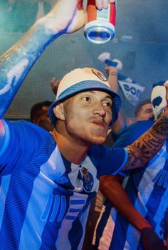 a man holding up a can in the air with other people around him and wearing blue shirts