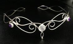 This magical, fairytale inspired wedding circlet is regal, elegant and bohemian wrapped into one fantastic package! I will fabricate this headpiece in sterling silver, featuring a glowing 10mm Moonstone with two side, 6mm Amethyst cabochons. This headpiece will fit behind threads for a comfortable fit. I use a jewelers stretch cord to tie off one end, and you tie the other end for a snug and secure fit to your head shape. You can gently manipulate to fit. Being Sterling silver, it will hold its Elegant Moonstone Jewelry For Festivals, Ethereal Adjustable Silver Jewelry, Ethereal Adjustable Jewelry For Festivals, Handmade Teardrop Crown Headpiece For Weddings, Mystical Crown Headpiece For Wedding, Whimsical Crown-shaped Jewelry For Weddings, Bohemian Silver Headpiece For Wedding, Silver Bohemian Headpieces For Wedding, Handmade Teardrop Crown Jewelry For Wedding