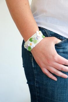 a woman wearing a bracelet with flowers on it's side and her hand in the pocket