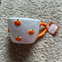 an orange and white coffee cup sitting on top of a carpet next to a tag