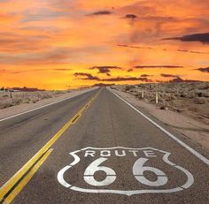 a route 66 sign painted on the side of an empty road at sunset with clouds in the sky