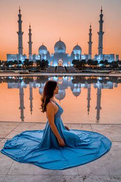 a woman sitting on the ground in front of a large body of water at sunset