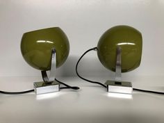 two green lamps sitting next to each other on top of a white table with black cords