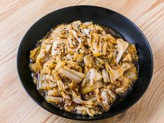 a black bowl filled with noodles and sauce on top of a wooden table next to a fork