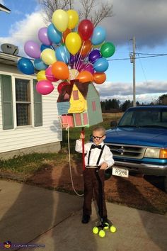 a young boy standing in front of a house with balloons attached to his head and wearing suspenders