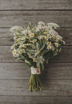 a bouquet of daisies and greenery tied to a wooden wall with wood planks in the background