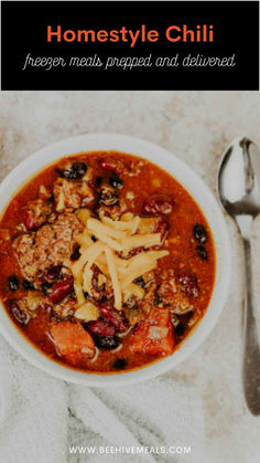 a bowl of chili with meat, beans and pasta in it next to a spoon