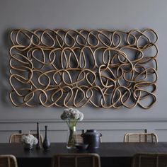 a large metal wall sculpture on the wall above a dining room table with chairs and vases