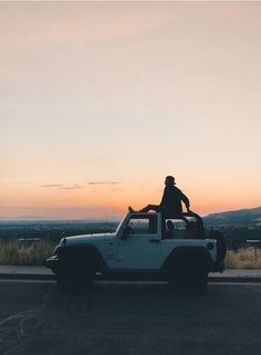 a person sitting on the top of a jeep in front of a mountain at sunset