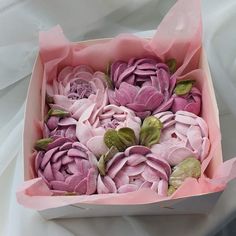 a pink box filled with purple flowers on top of a white sheet covered tablecloth