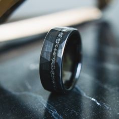 a wedding band with black and white diamond inlays sits on a marble surface