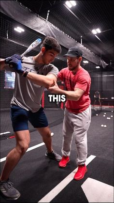 two men are practicing baseball in an indoor batting cage with the caption, this