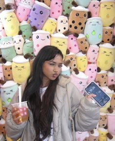 a woman holding a cell phone and drinking from a cup in front of a wall of stuffed animals