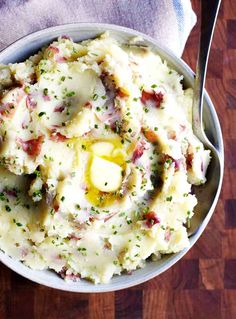 a bowl filled with mashed potatoes covered in butter and seasoning next to a fork