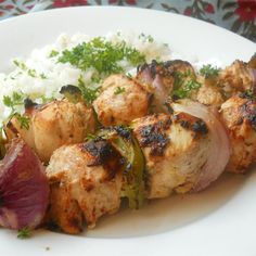 meat and vegetables on skewers with rice on a white plate, ready to be eaten