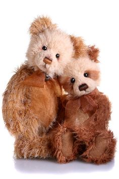 two stuffed teddy bears sitting next to each other on a white surface with one bear holding the other