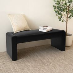 a black bench with a book on it next to a plant and a potted tree