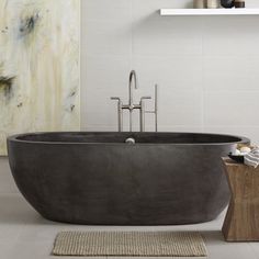 a bath tub sitting on top of a white floor next to a wooden block in front of a painting