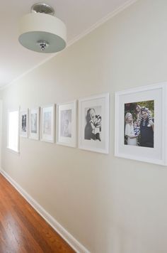 a hallway with pictures on the wall and wood flooring in front of white walls