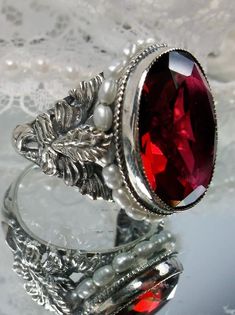 This detailed ring is an antique reproduction beautifully crafted in solid sterling silver. The lovely ring is set with a flawless man-made/simulated red ruby gemstone. The oval gem is 18mm long by 16mm wide. The inside of the band is marked 925 for solid sterling silver. Notice the intricate and detailed palm tree and floral design of the silver filigree setting and band. Tiny seed pearls create a beautiful outline for the gemstone. This is an exquisite rendition of an antique filigree ring. Victorian Ruby Jewelry For Collectors, Vintage Ruby Ring Stamped 925 For Formal Occasions, Victorian Ruby Jewelry Collectible, Antique Silver Garnet Jewelry, Silver Ruby Rings For Collectors, Ornate Ruby Rings Hallmarked, Victorian Red Ruby Ring In Sterling Silver, Victorian Engraved Ruby Ring As Gift, Collectible Silver Garnet Jewelry