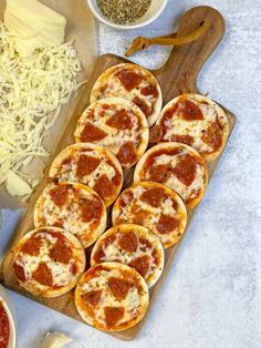 several small pizzas are on a cutting board with cheese and seasoning next to them