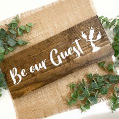 a wooden sign that says, be our guest on it next to some green leaves