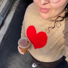 a woman with glasses holding a drink in her right hand and a red heart on the sweater