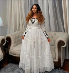 a woman standing in front of a couch wearing a white dress with black trims