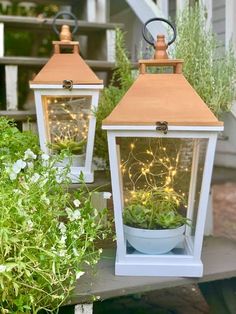 two white lanterns with plants in them on a porch