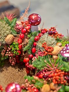 an assortment of christmas decorations and ornaments on a wooden surface with red berries, pine cones, evergreens, and other greenery