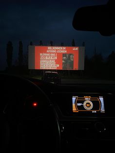 a car driving down a road at night with a large screen in the back ground