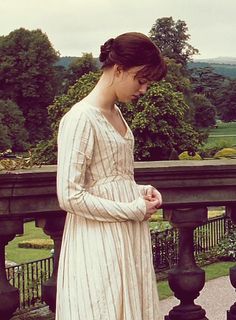 a woman in a white dress standing on a balcony looking down at her cell phone