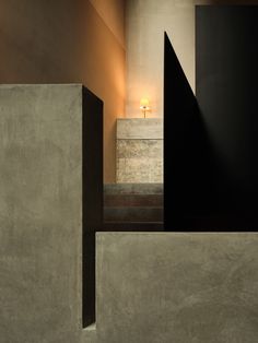 an empty room with concrete walls and steps leading up to the door, in front of a light that is on