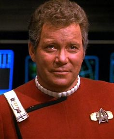 the man is wearing a red uniform and has a star trek badge on his collar